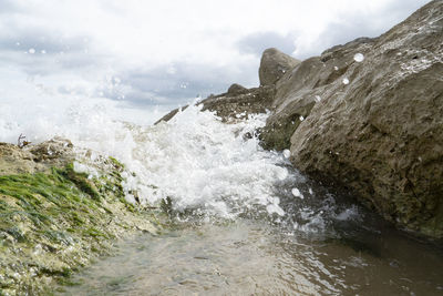 Sea waves splashing on rocks against sky