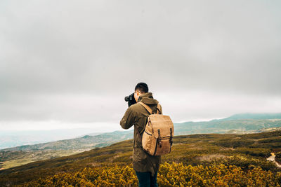 Rear view of man photographing while standing on field against sky