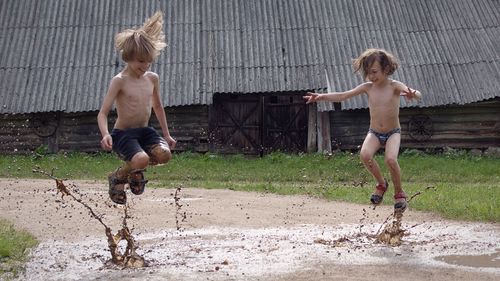 Full length of boys jumping in muddy water