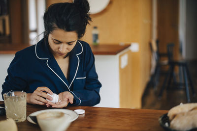 Woman taking medicine during breakfast while sitting at table