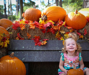 Girl smiling on bench by pumpkins at park during autumn
