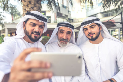 Man with brother and grandfather wearing dish dash taking selfie from phone outdoors