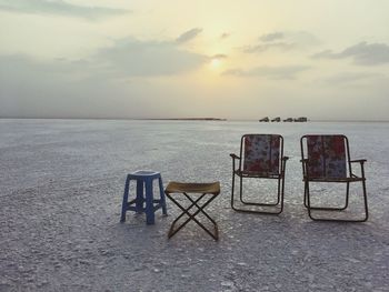 Chairs on beach against sky during sunset