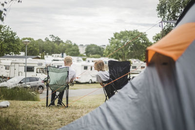 Siblings talking while sitting on chairs at camping site