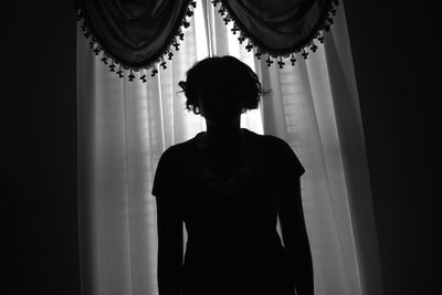 Rear view of silhouette woman standing against curtain