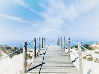 Empty wooden walkway leading towards sea against sky