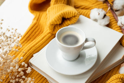 Cozy composition of warm yellow sweater, white books , cup of hot coffee and dry flowers , top view