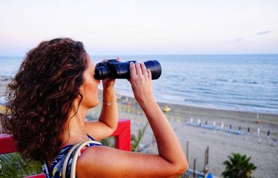 Side view of mature woman looking at sea through binoculars