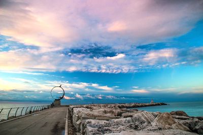 Walkway leading towards sea against cloudy sky at sunset