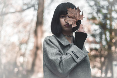 Portrait of woman covering face with maple leaf while standing on field