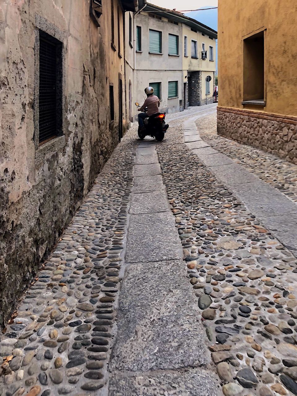 architecture, building exterior, built structure, one person, city, building, cobblestone, street, men, transportation, day, rear view, residential district, real people, adult, mode of transportation, direction, sitting, lifestyles, outdoors, riding, alley