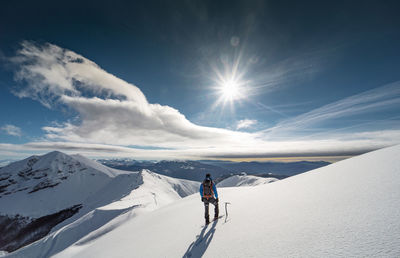 Rear view of mid adult man hiking on snowcapped mountain against cloudy sky
