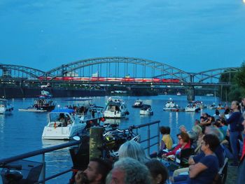 People sitting on bridge over river in city against sky