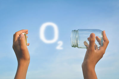 Cropped hands of woman holding jar against sky