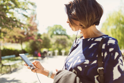 Businesswoman listening music through smart phone on footpath during sunny day