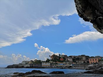 Buildings by sea against cloudy sky