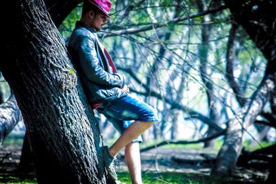 Full length of man sitting on tree trunk