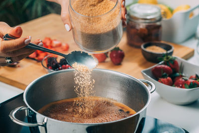 Woman cooking fruits and making homemade jam. putting brown sugar in the pot.