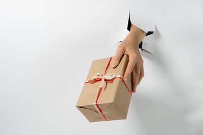 Close-up of female hand holding gift with ribbon through a torn white paper. creative present