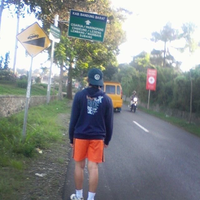 communication, text, lifestyles, western script, road, casual clothing, road sign, leisure activity, sign, tree, street, transportation, standing, guidance, front view, day, full length, holding