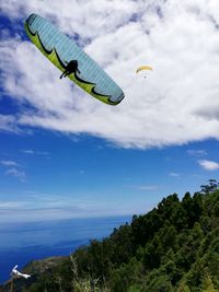 Low angle view of people flying over sea against sky