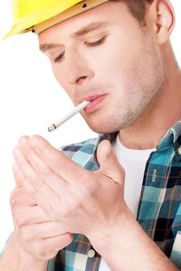 Close-up of engineer wearing hardhat smoking cigarette against white background