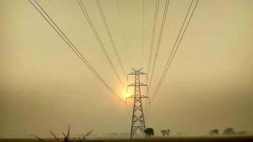 Low angle view of silhouette electricity pylons against clear sky