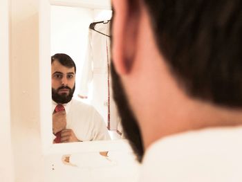 Man adjusting necktie while looking in mirror at bathroom