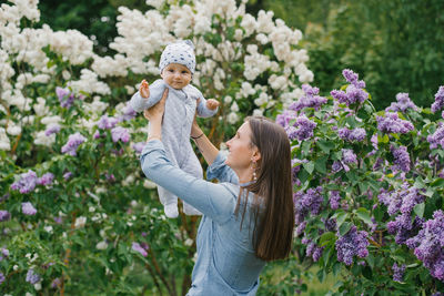 Happy european mother lifts up her little smiling son in her arms in the spring on a walk