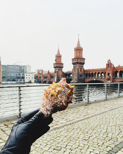 Hand holding a croissant  by river in city against sky