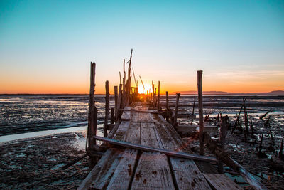 Wooden posts on beach against sky during sunset