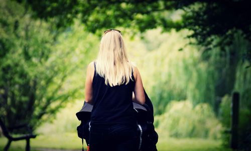 Rear view of woman with blond hair standing against trees in park