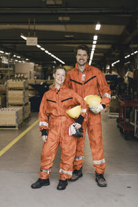 Portrait of smiling male and female coworkers in uniform standing at factory warehouse