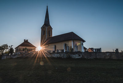 Church on field by building against clear sky