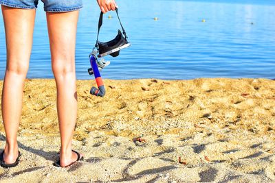 Low section of woman holding scuba mask at beach 