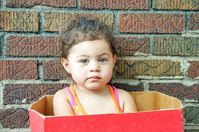 Close-up of girl sitting in box against wall