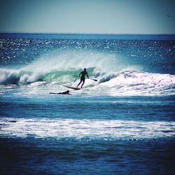 People surfing on wave in sea against sky