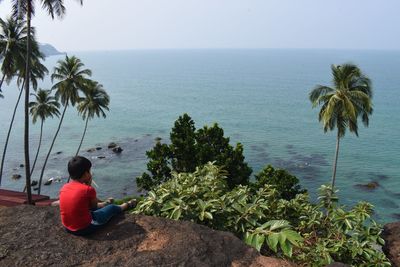 Rear view of man sitting by sea against sky