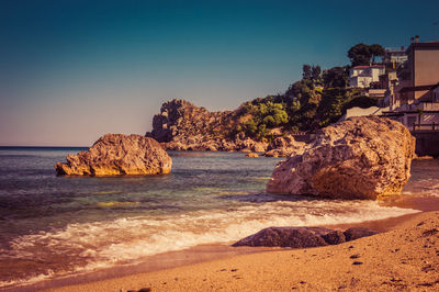 Rocks on beach against clear blue sky