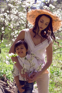 Woman in pink clothes and a straw hat stands with a child in a white shirt  blossoming apple orchard