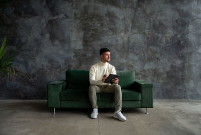 Young woman using laptop while sitting against wall