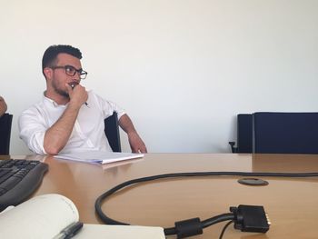 Serious man sitting at conference table against wall in office meeting