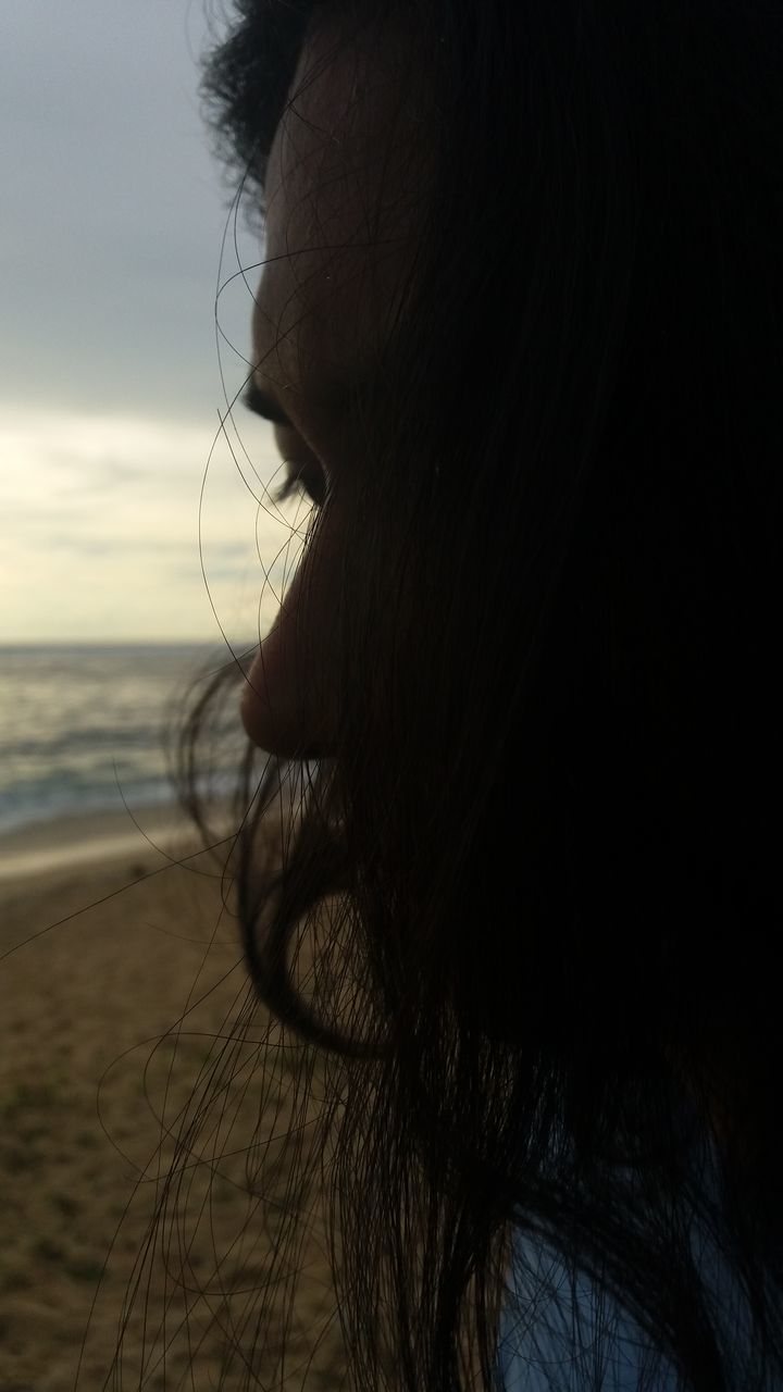 CLOSE-UP PORTRAIT OF WOMAN AT BEACH DURING SUNSET