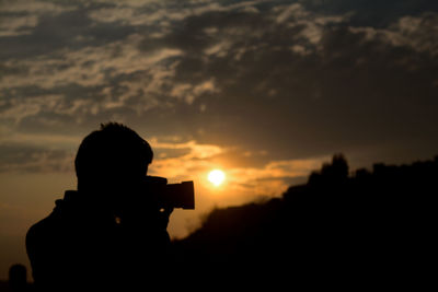 Silhouette man photographing against sky during sunset