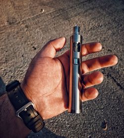 Cropped hand of man holding electronic cigarette on road