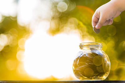 Close-up of hand holding coin over glass jar