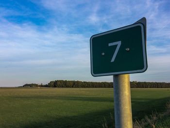 Road sign on field against sky