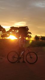 Silhouette person riding bicycle against sky during sunset