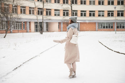 A cute girl walks through the snow in winter with a backpack and smiles