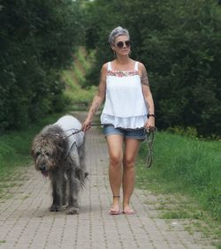 Full length of mature woman with dog standing on footpath against trees in park